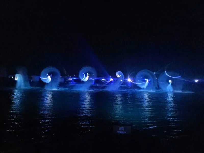 Hàng vận động viên jet ski chạy đội hình trên mặt biển trong show Symphony of the Sea, vệt sáng xanh kéo dài trên nước